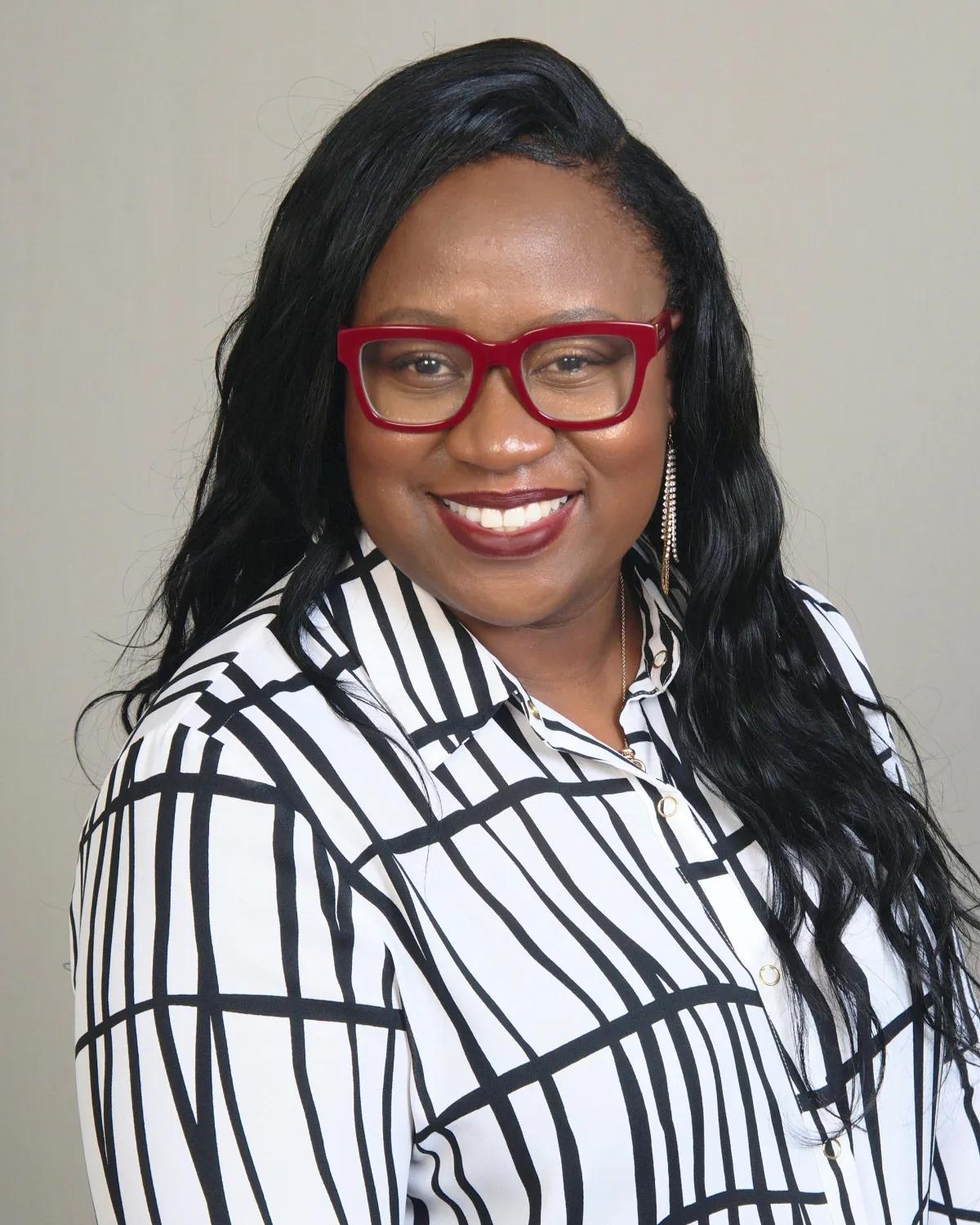 Professional headshot of Audrey Morison, founder of Midas Immigration Services, wearing red glasses and a striped blouse